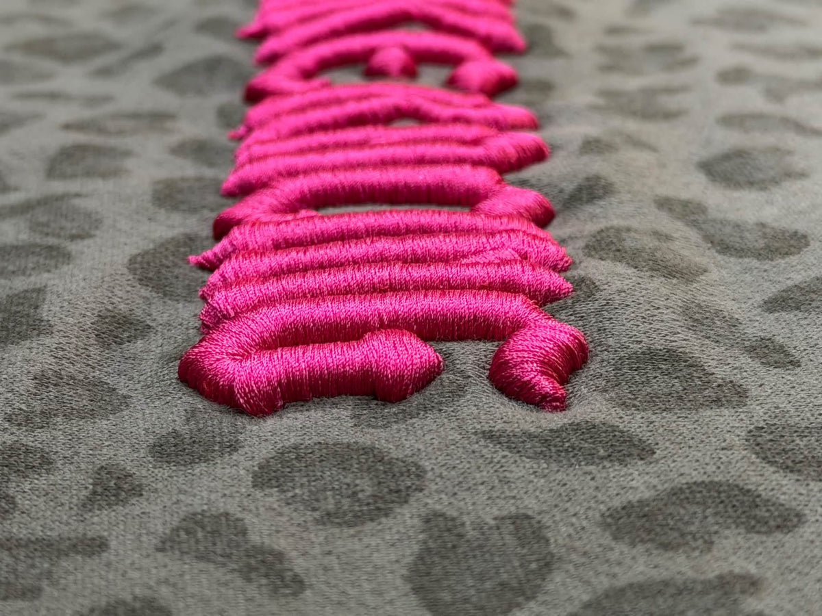 Close-up of the raised hot pink MKE Racing puff embroidery on leopard-print fabric.